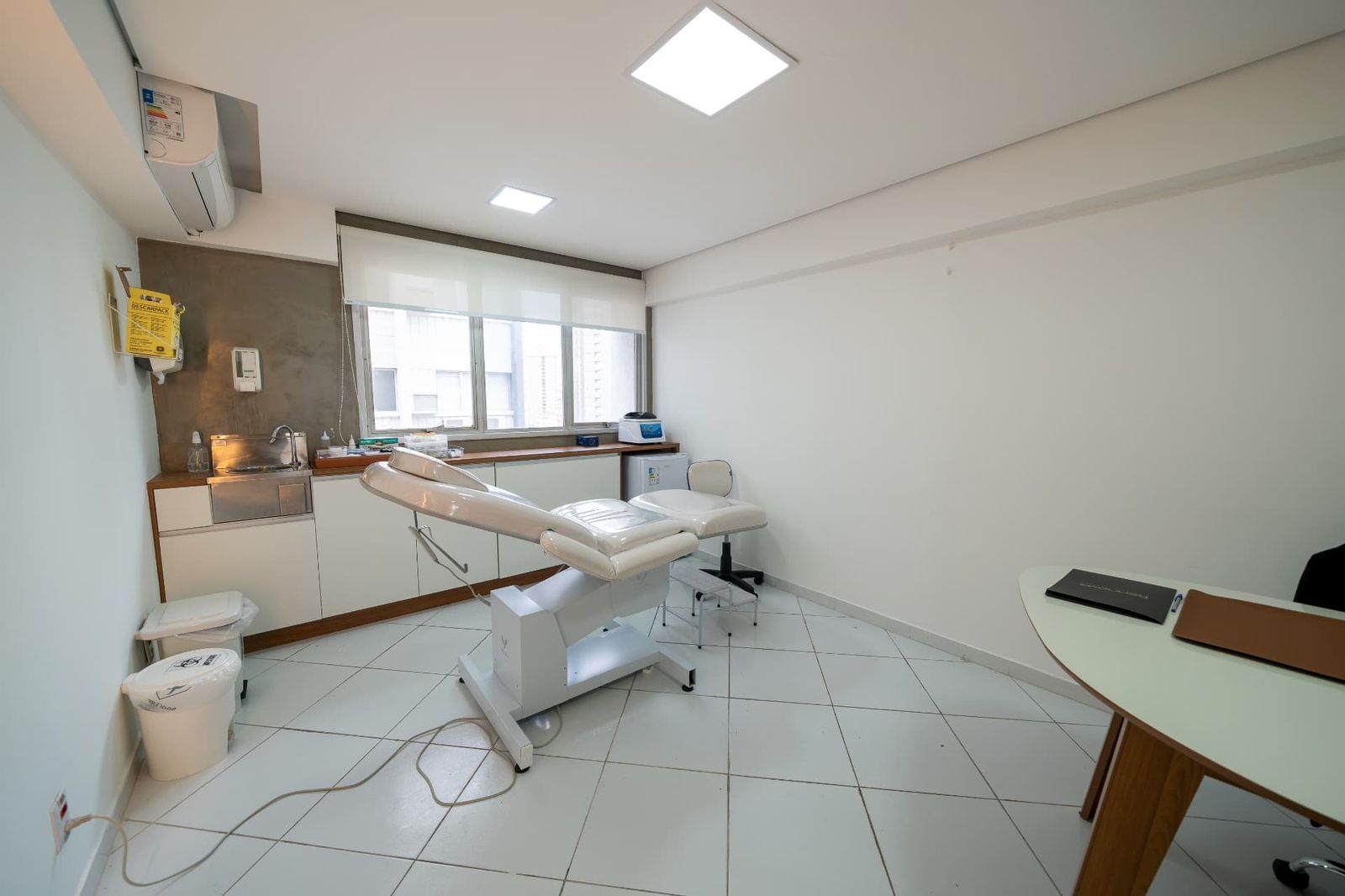 Sala clara com maca elétrica, pia e janela ampla