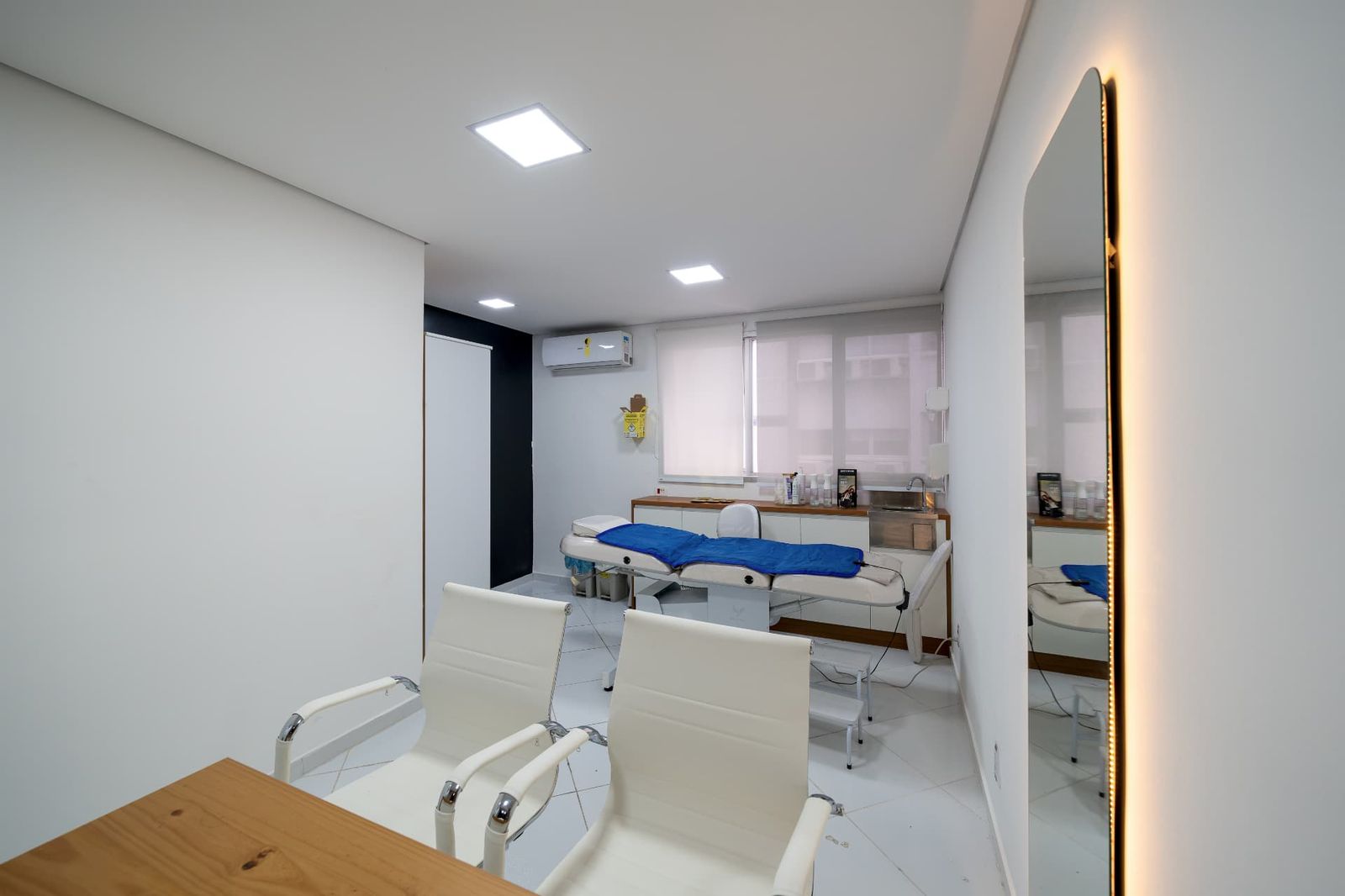 Sala de atendimento com maca, pia e espelho de corpo inteiro