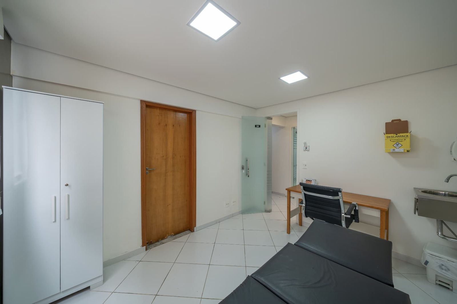 Sala ampla com maca, armário, pia e acesso ao corredor