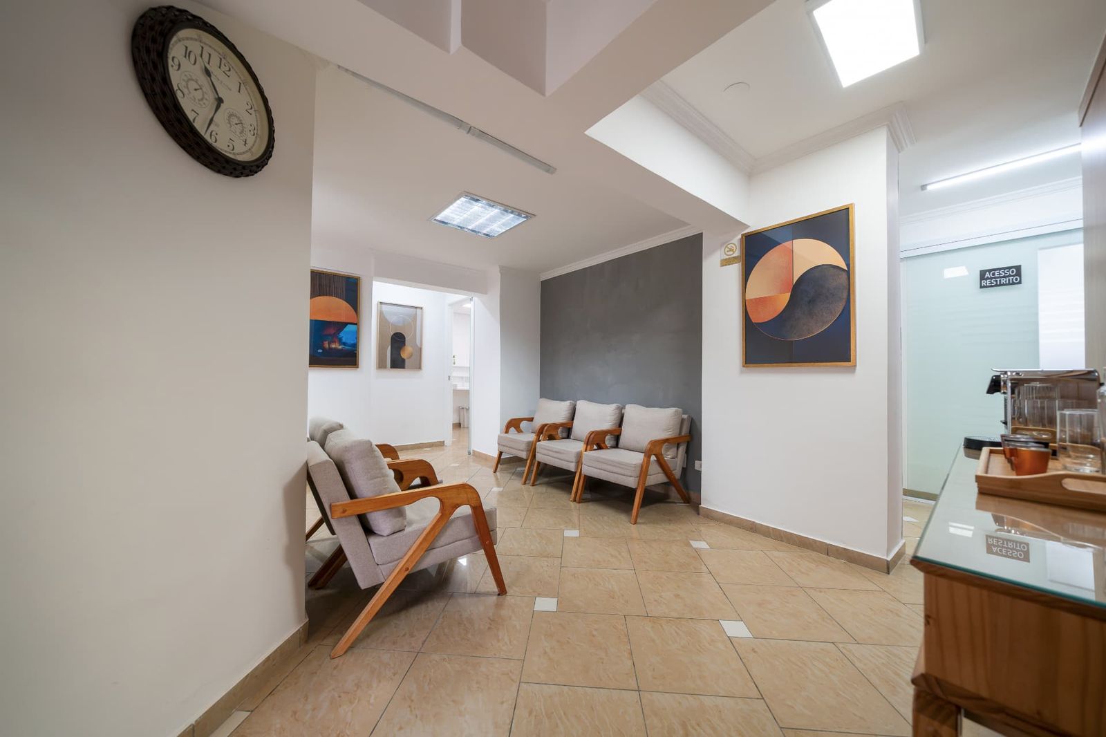 Sala de espera com poltronas, quadros e estação de café